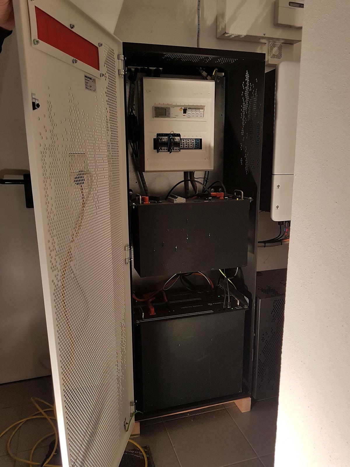 Geopende witte batterijkast met bovenaan een schakelpaneel en daaronder twee zwarte batterijmodules met gele bekabeling